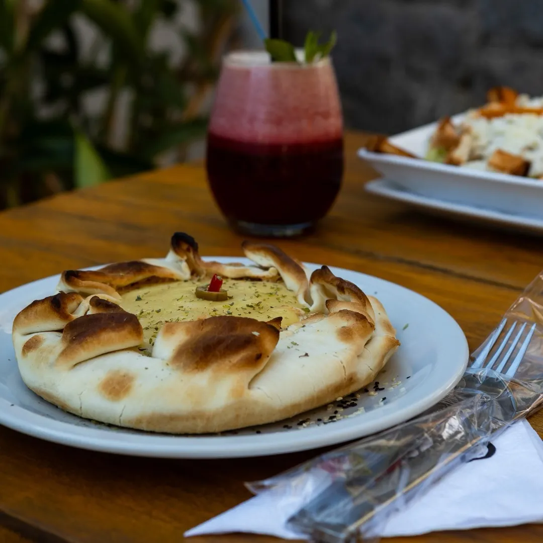 Fugazza horneada estilo rotisería junto a un jugo de frutos rojos.